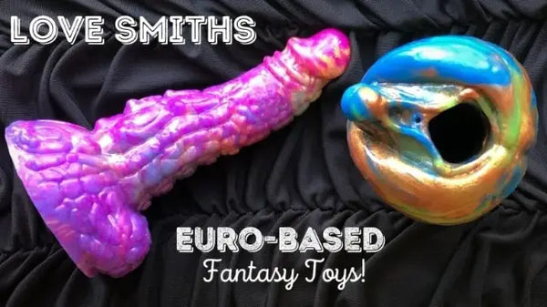 Promotional photo showing a purple fantasy dildo and a metallic blue–gold stroker displayed on black fabric, with text reading ‘Love Smiths – Euro-Based Fantasy Toys’.