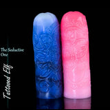 Dos masturbadores de silicona Tattooed Elf en posición vertical, en combinaciones de colores rosa y azul con blanco, mostrando sus ornamentados diseños de tatuajes de fantasía.