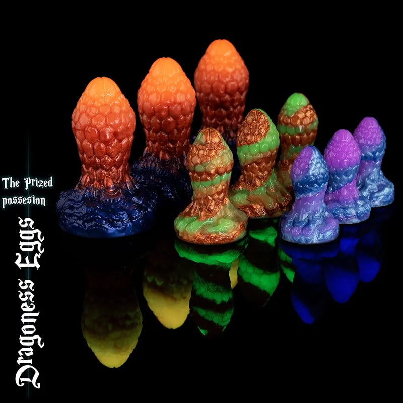 Collezione completa di plug anali fantasy Dragoness Eggs nelle taglie Cute, Herculean e Mammoth, con texture a scaglie di drago in silicone arancione metallizzato, marmo verde e spirale viola.