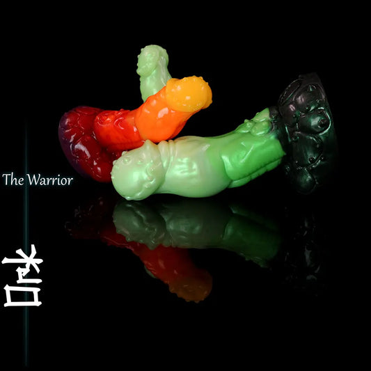 Multiple green, red and orange fantasy ork-inspired silicone dildos displayed on black reflective surface with sculpted creature texture and wide base.