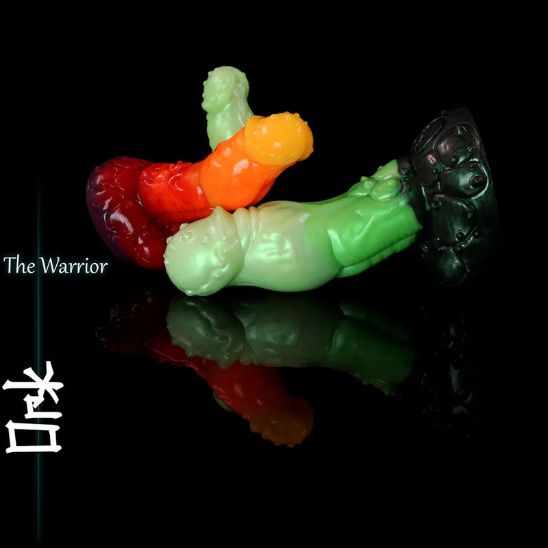 Multiple green, red and orange fantasy ork-inspired silicone dildos displayed on black reflective surface with sculpted creature texture and wide base.