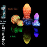 Plug anali fantasy Dragoness Eggs sotto luce e con effetto fosforescente, con plug anali in silicone a scaglie di drago testurizzate in vivaci miscele custom arancione, marmo verde e viola.