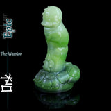 Green fantasy ork silicone dildo standing upright with textured creature details and sculpted base on black background.
